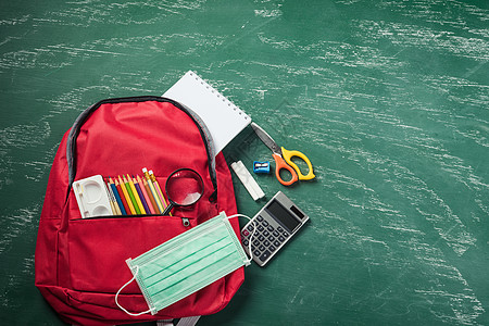 红色学校背包 放在绿色黑白板上 面罩防护和文具图片