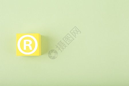 黄色玩具立方体上的白色商标标志 亮粉色绿色背景 带复制空间图片