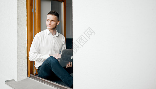 这家伙坐在房子窗台上 看外面 手拿着一台笔记本电脑图片