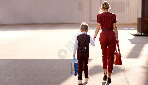 母亲和儿子在去新学年的路上带着袋子图片