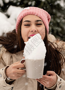 女人穿着温暖的冬衣 站在大圣诞树旁边露着户外 从杯子里舔雪幸福市场闲暇城市季节女性森林微笑假期庆典图片