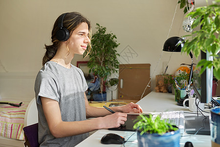 使用计算机和一张图形平板电脑坐在家中的耳机上的青少年男子图片