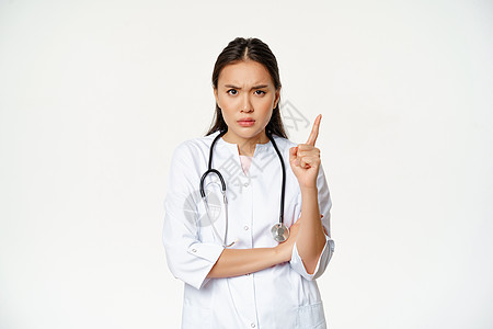 医生表示不赞成 责骂病人 愤怒的亚洲女医生摇着手指 皱起眉毛 对不良行为感到失望 站在白色背景上女士专家成人看门人工人感染医院职图片