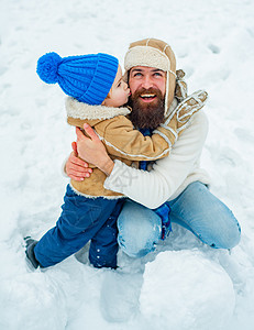 儿子在寒假拥抱他的父亲 爸爸和宝贝儿子一起在户外玩耍 快乐的孩子在白色的冬天背景下玩雪球图片