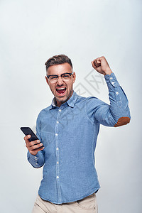 英俊和快乐的长胡子男成功肖像 身穿眼装 戴着智能手机 握着一只手紧握拳头而站在灰色背景下站立图片