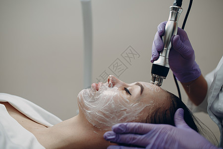 年轻女子在美容疗养所用电动设备进行电子RF提升面部按摩图片