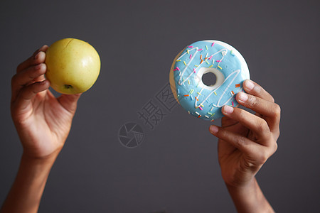 灰色背景下手持甜甜甜圈和苹果背景图片
