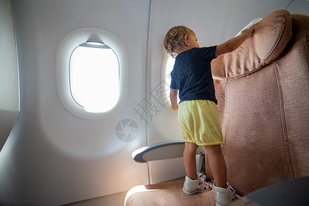 飞机上的小孩站在乘客座椅上很危险的地方 笑声座位微笑班级注意力航班窗户家庭生长婴儿旅行图片
