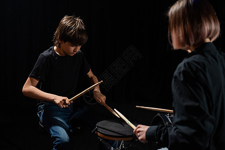 年轻的天主教女青年教男孩用黑人背景在工作室里打鼓 音乐学校学生 请讲作曲家艺术家黑色笔记鸡腿娱乐教学爱好天赋孩子图片