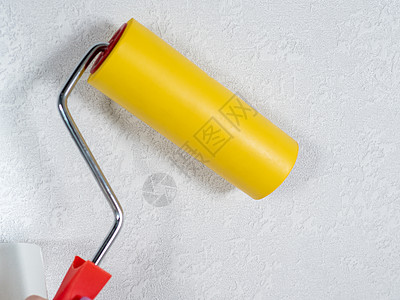 工具 用于平滑黄色墙纸的滚筒 浅色背景上带有红色手柄和黄色光滑喷嘴的油漆滚筒 在公寓里贴墙纸图片