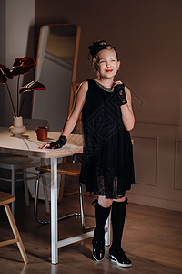 一个穿黑衣服的时装小女孩 在桌子附近的内地 站着派对裙子窗户收音机教育黑色孩子们风格头发手套图片