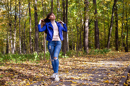 秋天公园的年轻美女 在阳光下照耀着黄树背景天空乐趣季节喜悦日落公园女性现实快乐森林图片