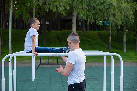 白人男子在游乐场的不平坦酒吧训练一个男孩 爸爸和儿子去户外运动横杆操场城市父亲动机手臂肌肉活力孩子们运动图片