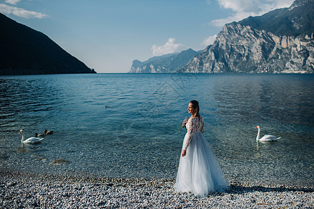 一名女性在意大利一座山和湖的背景下被拍到照片 TorboleTorbole 在Lake Garda湖的堤岸上行走山脉快乐连衣裙街图片