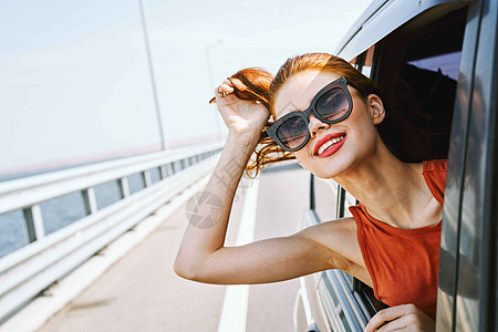 身戴墨镜的妇女在汽车窗外看望着的车窗 旅行生活方式窗户冒险司机朋友们假期游客晴天夫妻太阳镜蓝色图片