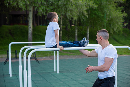 白人男子在游乐场的不平坦酒吧训练一个男孩 爸爸和儿子去户外运动力量横杆公园平衡父亲享受男性运动手臂活力图片