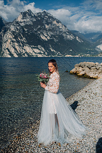 一名女性在意大利一座山和湖的背景下被拍到照片 TorboleTorbole 在Lake Garda湖的堤岸上行走蓝色山脉白色公主图片