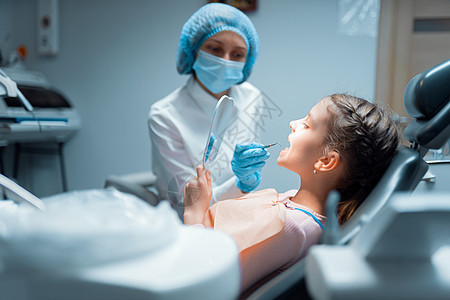小女孩病人和女牙医在牙科诊所治疗后 正在镜镜上检查牙牙的牙齿图片