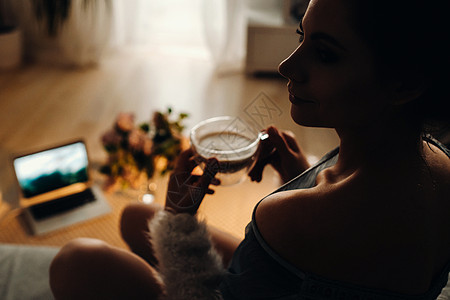 一个轻松的女孩在家喝咖啡看电影 家庭平静 女孩舒适地坐在沙发上喝咖啡乐趣房间服务微笑电脑主妇成人电视幸福笔记本图片