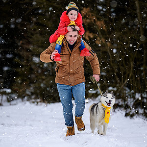 与主人和他的女儿一起穿着黄色围巾的Husky在冬季森林中行走图片