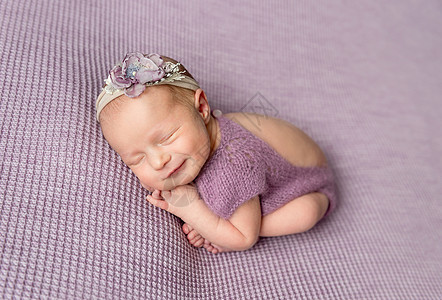 穿紫体服的新生小女婴睡觉时微笑着笑容图片