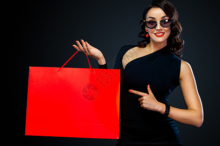 黑周五商店的销售概念 戴墨镜的购物女孩拿着红包在黑暗背景中被孤立 女性指着看左侧复制空间女士头发购物中心女孩黑发快乐购物成人奢华图片