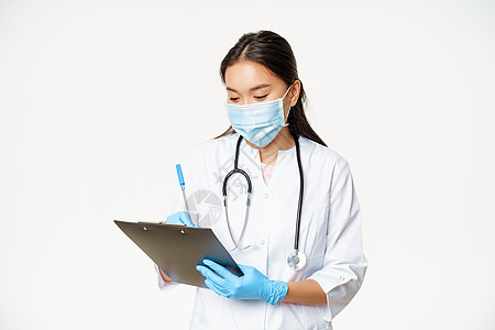 女性亚洲女医生在剪贴板上记录病人信息 写处方或诊断 用橡胶手套 白色背景的面罩站立在医疗面具中广告预防成人感染工人社交诊所药品口图片
