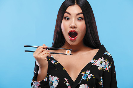 惊异的亚洲女人在蓝底吃寿司和卷子 黑色星期五寿司销售图片