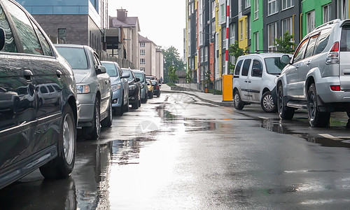 在雨天没有人停着车的城市街道 路上下雨 雨和车 多雨的城市街道上停放汽车的背景 对称停放的汽车前灯水坑沥青细雨驾驶车辆运输交通行图片