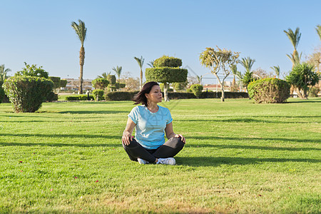 中年妇女坐在草地上的莲花姿势和闭着眼睛冥想的中年妇女成人晴天运动专注瑜伽活力娱乐女性公园训练图片