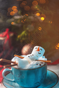 圣诞背景 一个棉花糖男人躺在一个杯子里 杯子里放着可可 背景是一棵圣诞树 上面放着玩具花环和礼物假期微笑糖果新年家庭魔法雪花棉花图片