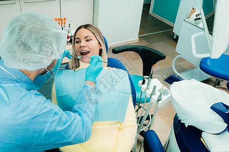 一名戴保护面罩的牙医坐在他旁边 在牙科办公室为病人治疗女士专家磨牙医生检查药品康复牙齿考试程序图片