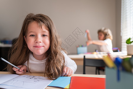 有趣的快乐女学生在课堂上写笔记 孩子们在学校的教室里 小学生坐在书桌边看镜头呢 (笑声)图片