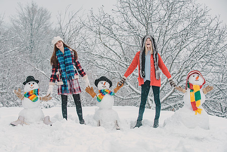 一群女孩在户外堆雪人 学生冬季聚会和圣诞节庆祝活动 两个快乐的年轻女人和雪人玩得很开心 圣诞快乐和新年快乐图片