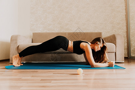 留着长发的年轻女性 穿着黑色运动服的健身教练 在家里的瑜伽垫上做伸展运动和普拉提 女性健身瑜伽常规概念 健康的生活方式 和谐与冥图片