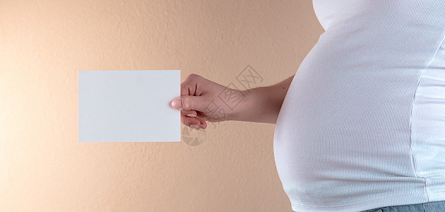 穿着白色短袖圆领汗衫 手持空纸的孕妇腹部的近视图图片