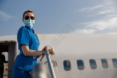 蓝制服空姐的肖像 太阳镜和防护面罩 在白天站在空中看着照相机并站立在空中图片