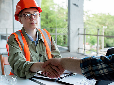 一位戴着安全帽的男工程师和一位女建筑工程师握手 准备在一个建筑项目上合作图片