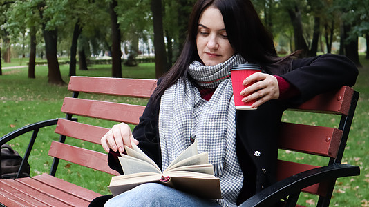 穿牛仔裤 大衣和围巾的年轻女子在公园长椅上看书 独自在户外喝咖啡或其他热饮女孩街道寂寞闲暇知识文学女性杯子乐趣自由图片