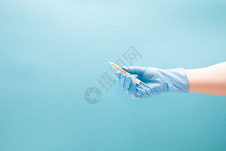 蓝色一次性医疗手套中的女性手握着一个汞温度计 蓝背景空间复制件间距图片