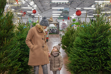 母亲和女儿在商店里选一棵圣诞树家庭大衣背景店铺闲暇孩子们市场女士孩子微笑图片