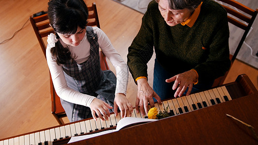 一个小女孩在音乐课上弹钢琴 一位老师帮助她 高角度图片