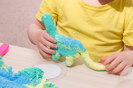 孩子在桌子上用聚合物颗粒玩橡皮泥 用小球做成的原始橡皮泥 孩子用橡皮泥玩恐龙 在家里和孩子玩什么手工业面团幼儿园游戏童年乐趣运动图片