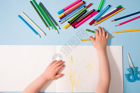 一个小孩用铅笔在相册 复制空间 顶视图 蓝色背景 铅笔 蜡笔 剪刀和桌子上的孩子的手上画画小样儿童家庭天赋学校艺术女孩幸福童年教图片