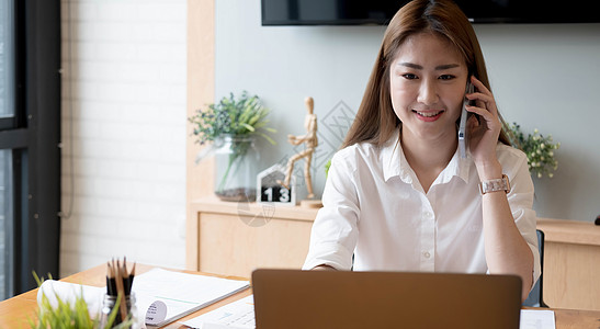 微笑的亚洲女性在笔记本电脑上工作时打电话给财务会计号码 文书工作统计月报技术经济人士电话金融桌子图表文档预算商业图片