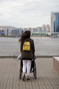 年轻女子与残疾男子一起坐在轮椅轮椅上行走的近视图片