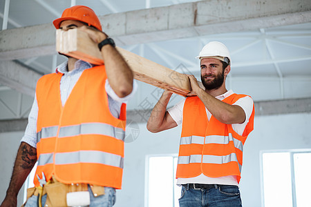 两名青年男子建筑工人在建筑工地上搬运木板 特写安全头盔反光工作领班男性职业相机木头衣服图片