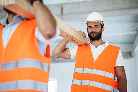 两名青年男子建筑工人在建筑工地上搬运木板 特写头盔背心成人实习生男性工作衣服男人木材工人图片