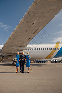 在阳光明媚的一天 驾驶员和两名身着蓝色蓝制服的空姐站在飞机前站在一起全镜头图片
