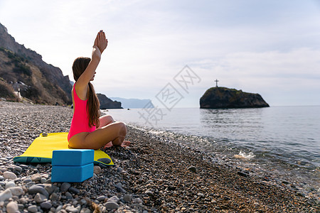 年轻漂亮的白种女人 留着长发 身着粉红色泳衣 日出时分在海边的海滩上练习健身 普拉提和现代瑜伽 健康的生活方式 冥想的概念 选择图片